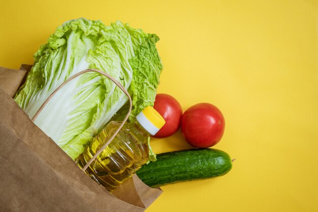 Bolsa de papel con verduras y aceite sobre un fondo amarillo.