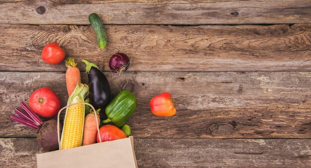 Una bolsa de papel con verduras esparcidas sobre un fondo de madera. Espacio para texto