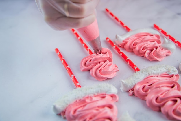 De la bolsa de pastelería el pastelero exprime un merengue en zigzag sobre pergamino blanco y un stic rojo