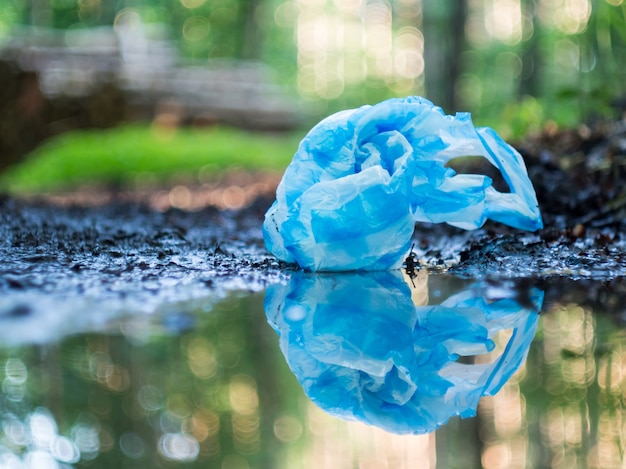 Foto bolsa de plástico azul ensuciando el bosque, reflejándose en un charco después de la lluvia. concepto de ecología, reciclaje y contaminación plástica.