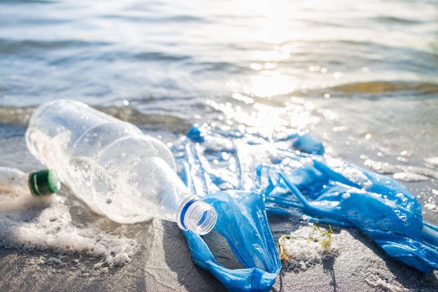 Bolsa de plástico y botellas en la playa, la orilla del mar y el concepto de contaminación del agua.