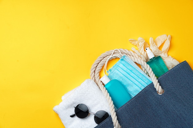 Bolsa de playa azul con accesorios de playa y máscara protectora sobre fondo amarillo