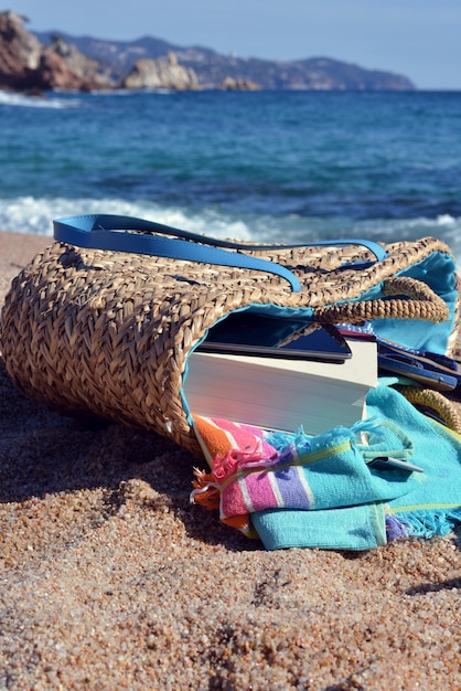 Bolsa de playa con un libro y un teléfono y gafas de sol acompañados de una estrella de mar.