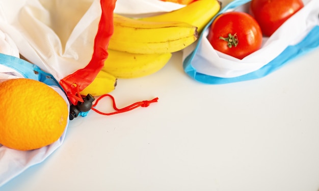 Bolsa de productos textiles reciclados de plástico sin residuos para llevar frutas (naranja, limón, tomate y un plátano) o verduras, superficie blanca vista superior. copyspace de maqueta