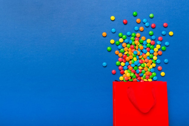 Bolsa de regalo de papel de compras en la esquina llena de dulces tradicionales variados cayendo sobre fondo de color con espacio de copia Concepto de venta de felices fiestas