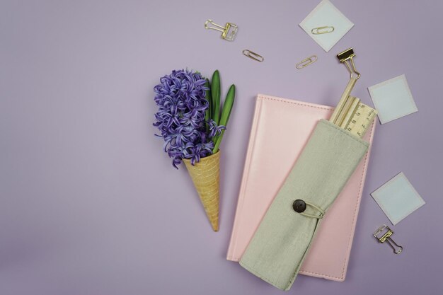 Una bolsa rosa con flores moradas y un lápiz en ella se asienta sobre un fondo morado.