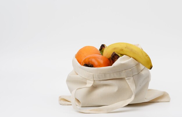 Bolsa textil beige con frutas frescas sobre un fondo blanco, lugar para una inscripción, cero residuos