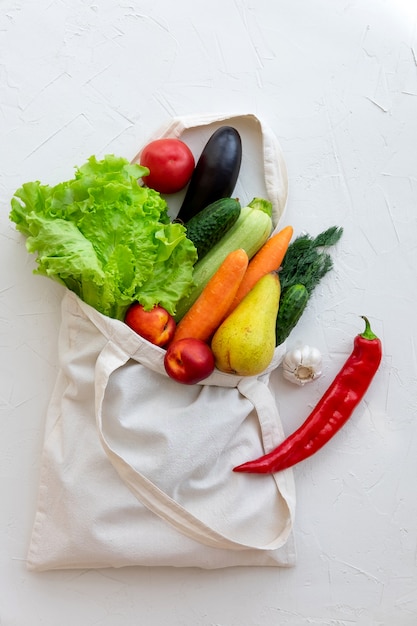 Bolsa de textil llena de verduras y frutas, vista superior en blanco.