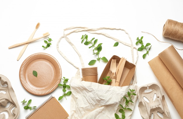 Bolsa de textil y vajilla desechable de papel artesanal marrón, hojas de menta verde sobre un fondo blanco