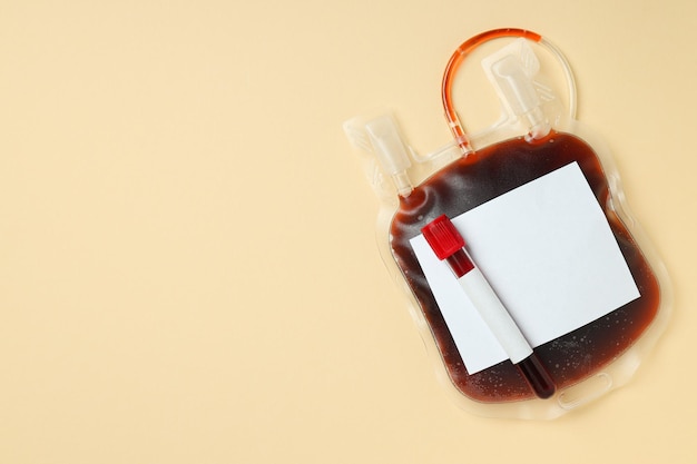 Foto bolsa y tubo de ensayo con sangre de donante en fondo beige espacio para el texto