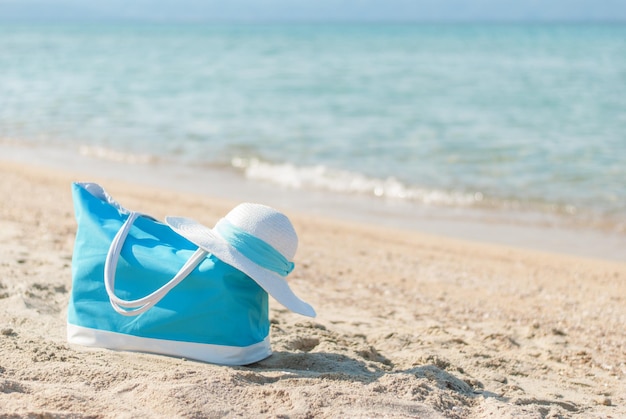 Bolsa turquesa e chapéu branco na praia.