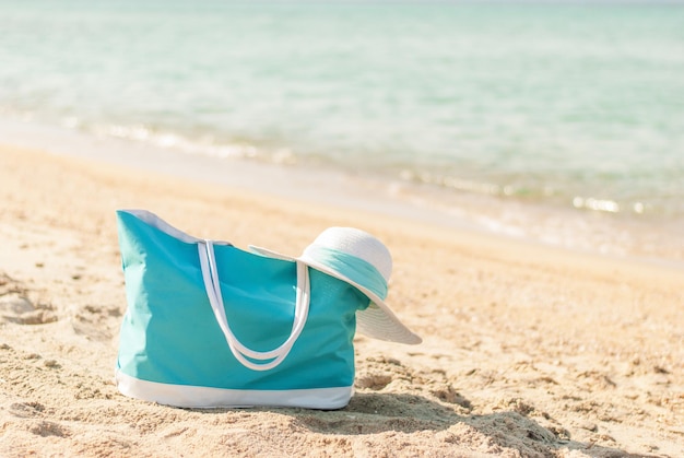 Foto bolsa turquesa y sombrero blanco en la playa.