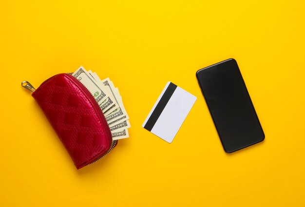Bolsa vermelha com notas de cem dólares, cartão do banco, smartphone em amarelo.
