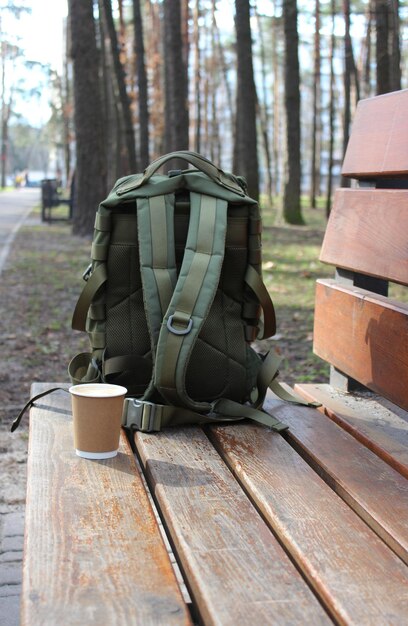 Foto una bolsa de viaje con correas cubre una taza de café de papel del viento en un banco del parque