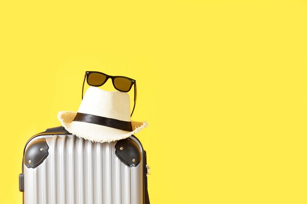 Bolsa de viaje, equipaje, sombrero de paja y gafas de sol sobre fondo amarillo con espacio de copia. maleta, sombrero, gafas de sol negras aisladas sobre fondo amarillo. Concepto de viajes de verano.