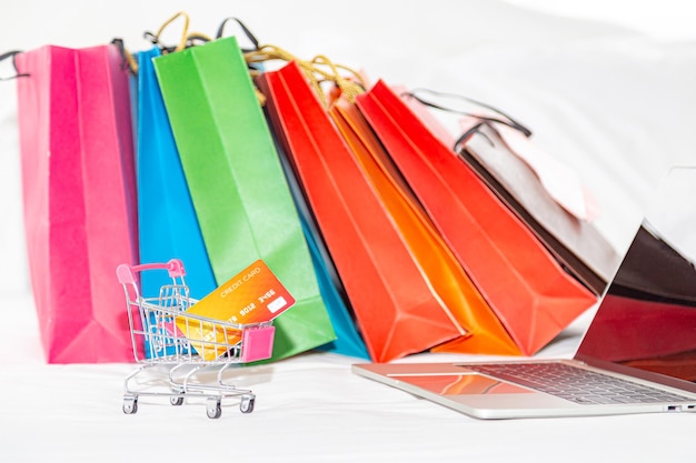 Bolsas de compras multicolores por carrito de compras en miniatura y portátil sobre fondo blanco