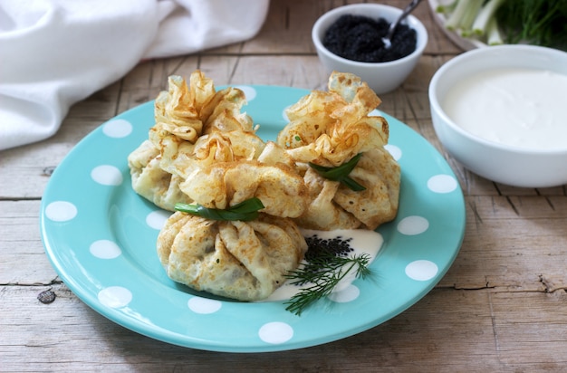 Bolsas de panqueques rellenos de arenque, servidos con caviar, crema agria y eneldo sobre un fondo de madera. Estilo rústico