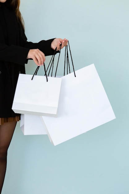 Bolsas de papel blancas vacías en la mano de una mujer joven y bonita haciendo compras en ropa negra de estilo casual