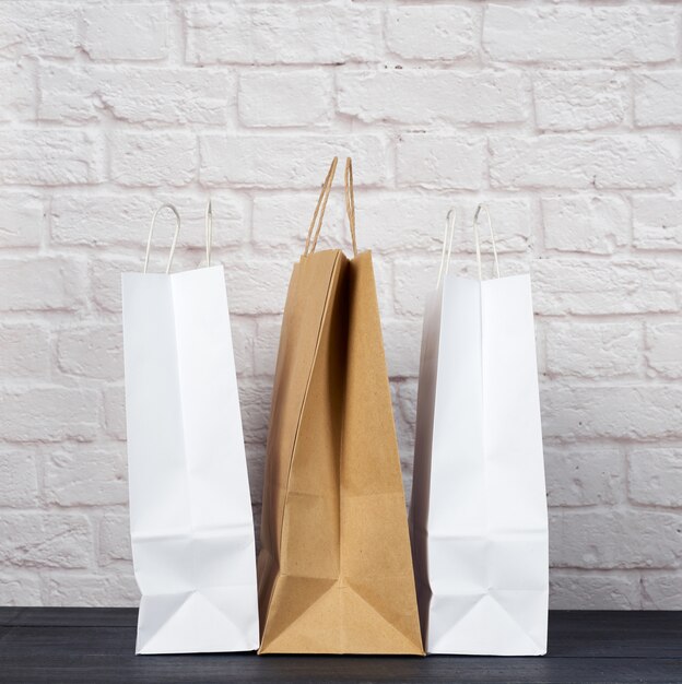 Bolsas de papel blanco y marrón con asas sobre fondo de pared de ladrillo blanco