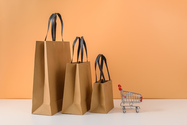 Bolsas de papel y carrito de compras o carro en mesa blanca y pared de color naranja pastel