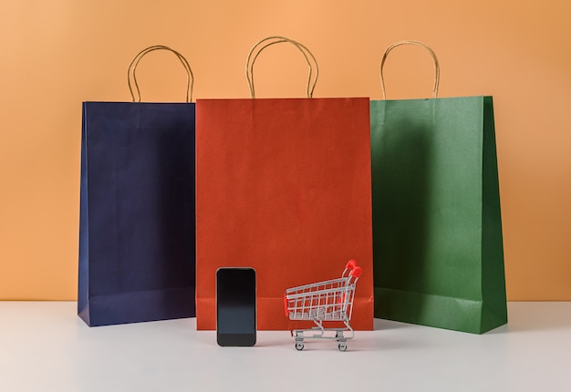 Bolsas de papel y carrito de compras o carro con teléfono en mesa blanca y pastel