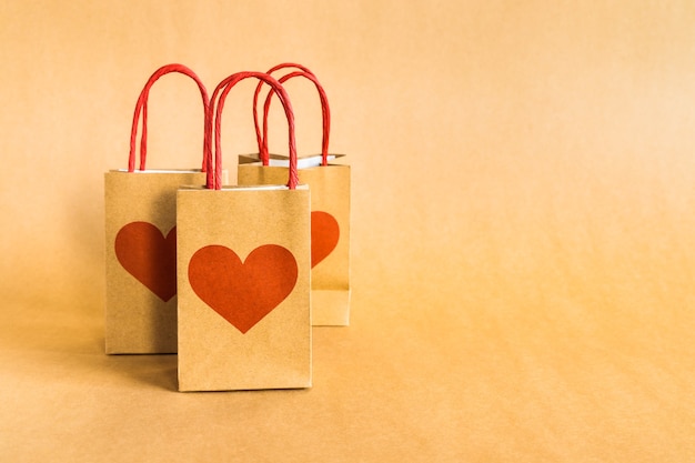 Bolsas de papel de compras con estampado de corazón sobre un fondo rojo.