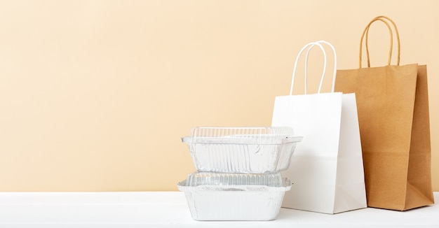 Bolsas de papel y envases de comida en el cuadro blanco. Servicio de comida a domicilio. Comida para llevar en envases de papel de aluminio, cartón vacío Paquete de papel.