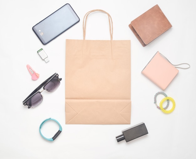 Bolsas de papel y muchas compras de gadgets y accesorios sobre un fondo blanco: gafas de sol, teléfono inteligente, pulsera inteligente, banco de energía, memoria USB, billetera. Concepto de consumidor. Vista superior.