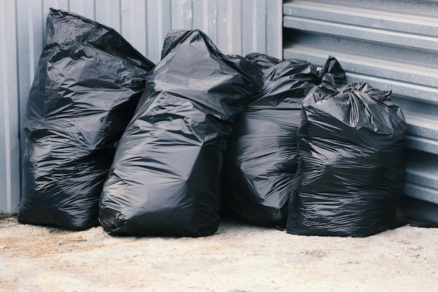 Bolsas de plástico de basura negras se encuentran cerca de una cerca de metal Eliminación de residuos o vertedero