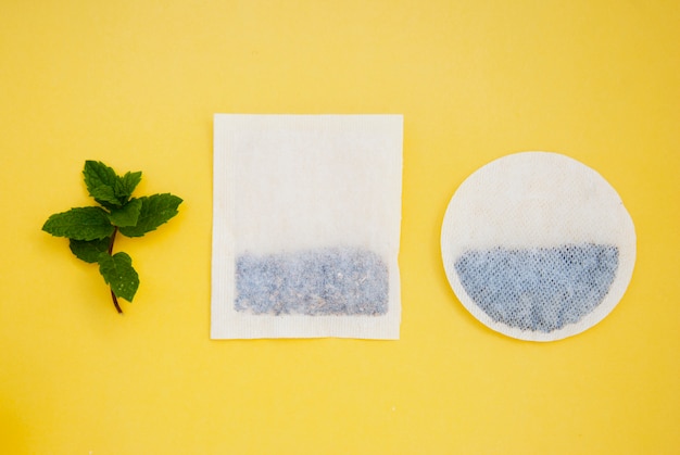 Bolsitas de té redondas y cuadradas en hojas amarillas y de menta, con copyspace. Bebidas y bebidas.