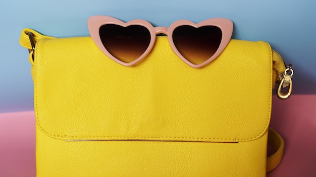 Bolso amarillo y gafas de sol en forma de corazón sobre fondo rosa y azul - imagen de verano