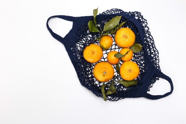 Bolso azul con mandarinas sobre un fondo blanco.