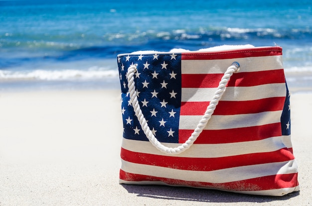 Foto bolso con colores de la bandera americana cerca del océano en la playa de arena