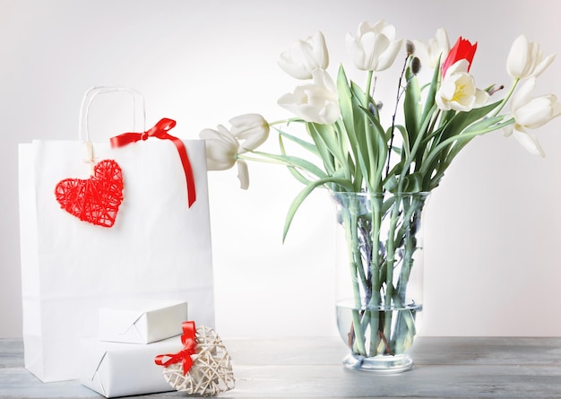 Bolso de compras, corazón rojo y cinta, regalo y ramo de tulipanes de ramo blanco en un jarrón sobre fondo blanco. Cumpleaños, Día de la Madre, San Valentín, Día de la Mujer