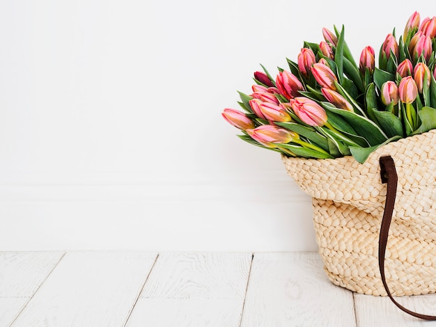 Bolso de compras ecológico tejido con tulipanes frente a un fondo de pared blanca