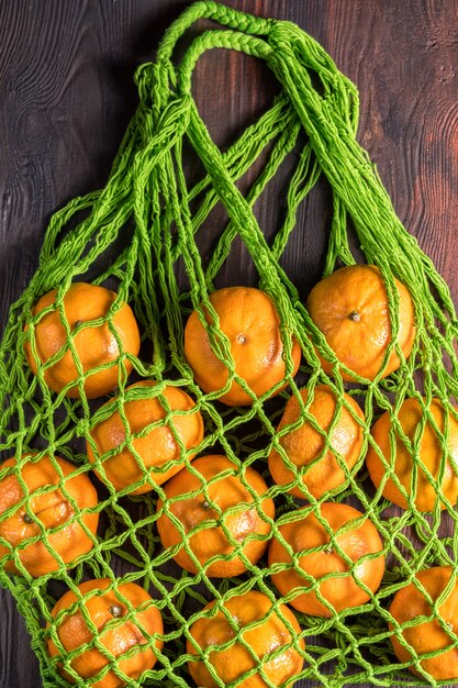 Bolso de compras de malla con naranjas frescas en marrón. Vista superior