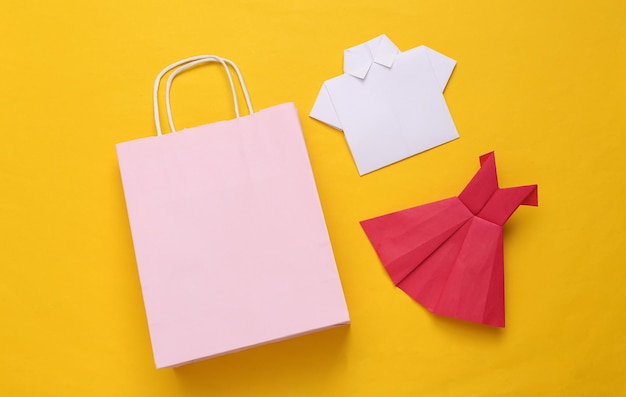 Bolso de compras con vestido de origami y camisa sobre un fondo amarillo Concepto de compras