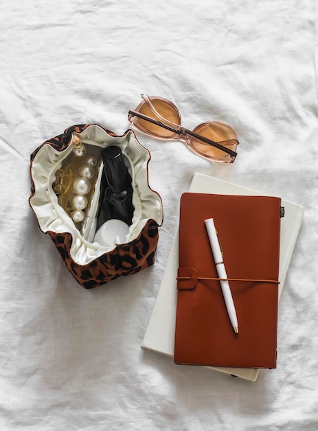 Bolso cosmético de impressão de leopardo com cosméticos coberto de couro, óculos de sol de notebook em um fundo claro, vista superior