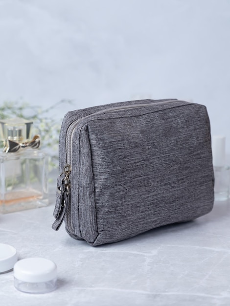 Bolso cosmético gris sobre una mesa de piedra con flores y perfume en el fondo