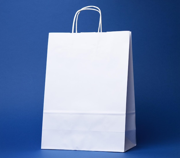 Foto bolso de papel branco descartável com alças em fundo azul de perto