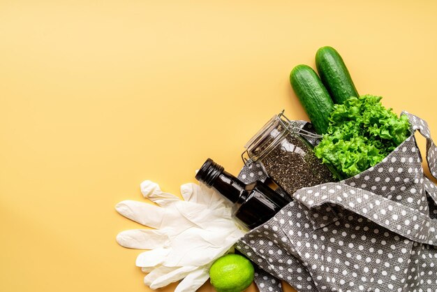 Foto bolso ecológico com vegetais verdes, sementes de chia, luvas e azeite de oliva, vista superior em fundo laranja com espaço para cópia