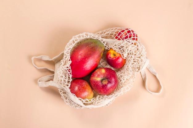 Bolso de hilo de rejilla beige con frutos rojos sobre fondo beige.