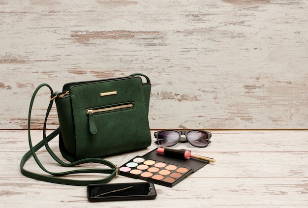 Bolso de mujer verde, gafas de sol, teléfono, sombra de ojos y lápiz labial