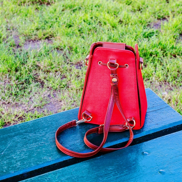 Foto bolso rojo brillante se encuentra en un banco de madera azul.