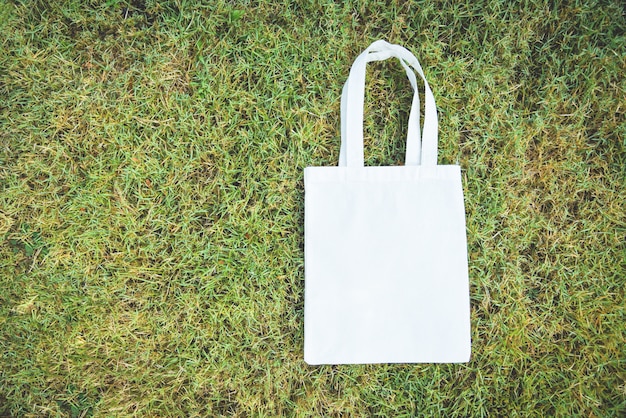 Bolso de tela ecológico de tela blanca en tela de lona bolsa de compras sobre fondo de hierba verde / Cero desperdicio Use menos plástico, digamos que no hay problema de contaminación de la bolsa de plástico