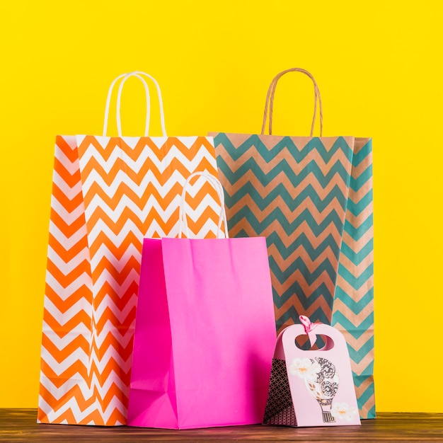 Bolsos de compras coloridos con diseño en la tabla de madera contra fondo amarillo