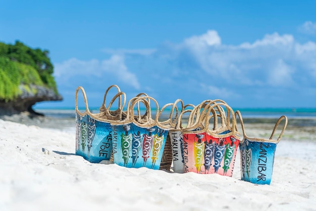 Bolsos de mujer de mimbre de colores en el estilo típico de Zanzíbar en la playa de arena blanca cerca del océano turquesa de la isla de Zanzíbar, Tanzania, África Oriental, cerrar