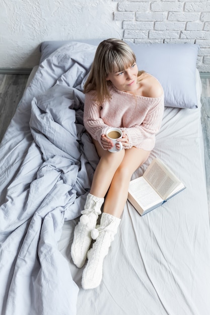 Bom dia com café. Jovem mulher na cama com copo