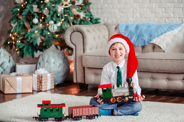 Bom dia, menino feliz, presente de trem de brinquedo sob a árvore de natal em uma manhã de ano novo