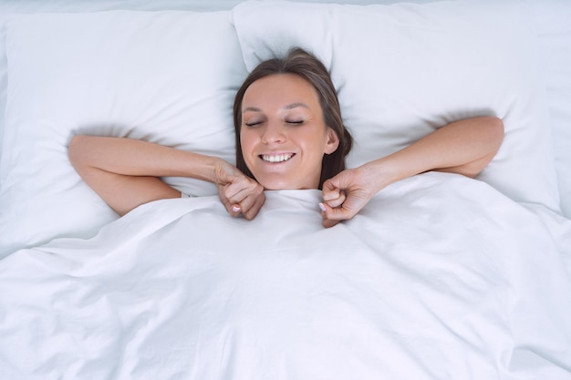 Foto bom dia vista de cima de uma bela jovem acordando feliz na cama branca dia de folga do trabalho